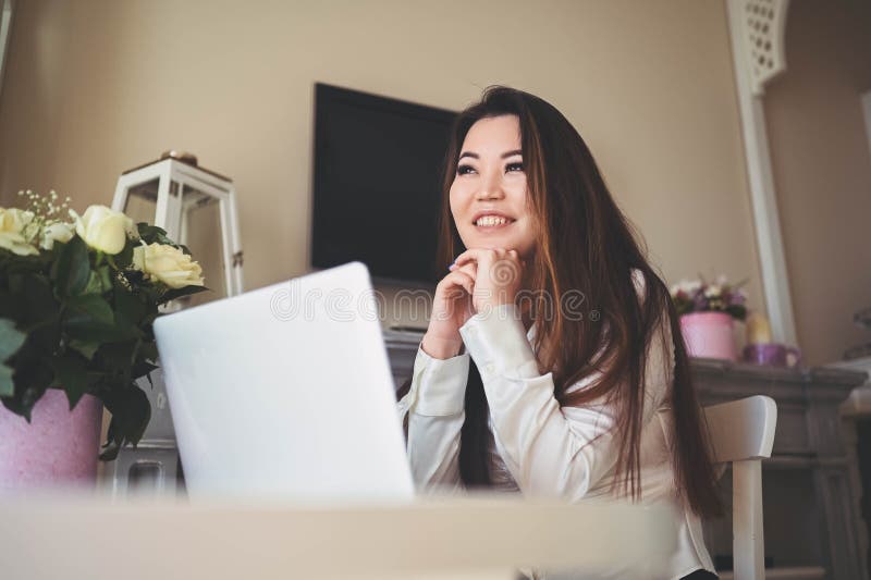 En ung, vacker affärskvinna som arbetar online med en bärbar dator placerad vid bordet på hemkontoret. leende fotografering för bildbyråer