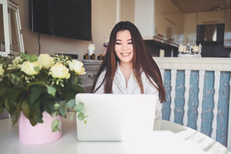 En ung, vacker affärskvinna som arbetar online med en bärbar dator placerad vid bordet på hemkontoret. leende royaltyfri bild