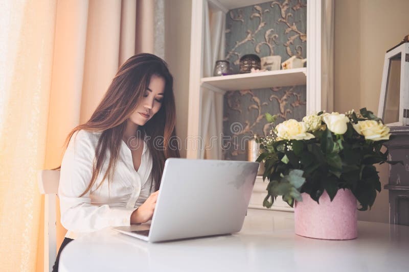 En ung, vacker affärskvinna som arbetar online med en bärbar dator placerad vid bordet på hemkontoret. leende fotografering för bildbyråer