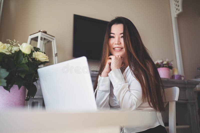 En ung, vacker affärskvinna som arbetar online med en bärbar dator placerad vid bordet på hemkontoret. leende arkivbild