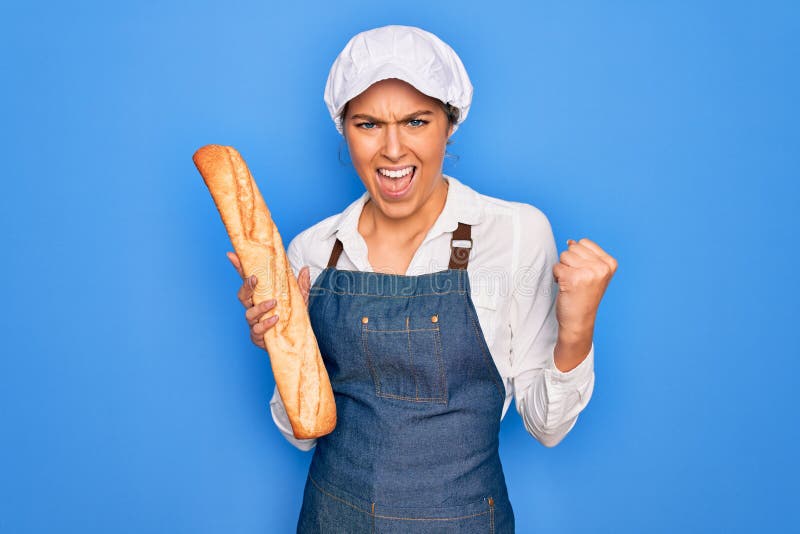 En ung, vacker, blond bakerkvinna med blå ögon som håller en limpa av hemmade färska bröd irriterad och frustrerad skrik med ilska royaltyfria bilder