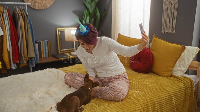 En ung vacker kvinna med enmajshuvud tar en själfik på sängen medan hon leker med sin hund i ett sovrum royaltyfri foto
