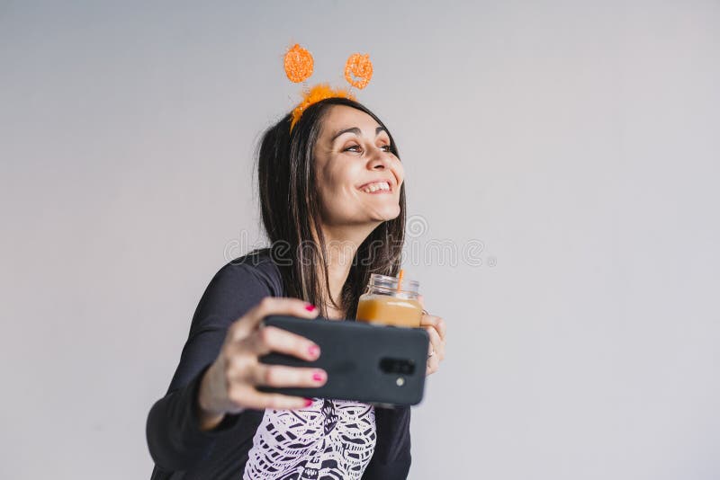 En ung vacker kvinna som dricker apelsinjuice och tar en selfie med mobiltelefon. Med ett svart och vitt skelett arkivbilder