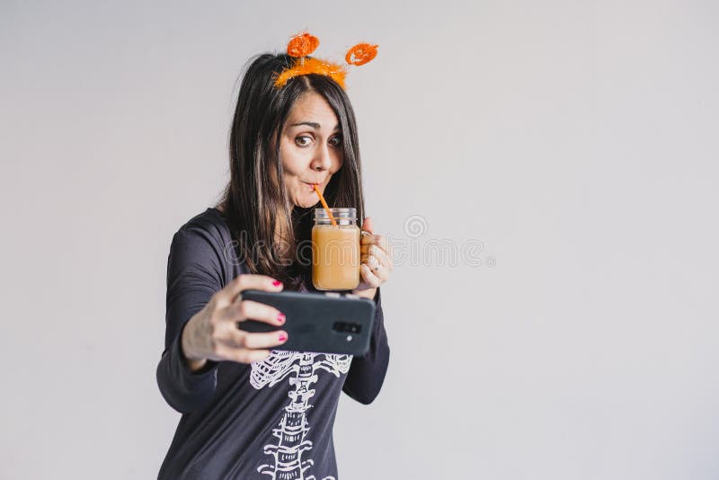 En ung vacker kvinna som dricker apelsinjuice och tar en selfie med mobiltelefon. Med ett svart och vitt skelett arkivbild