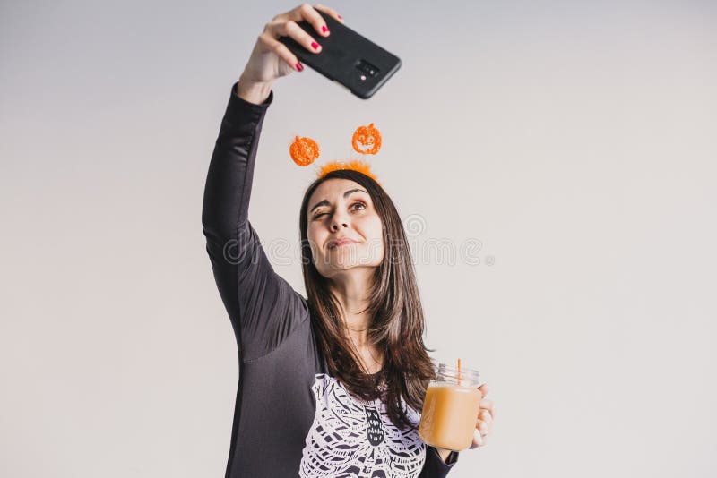 En ung vacker kvinna som dricker apelsinjuice och tar en selfie med mobiltelefon. Med ett svart och vitt skelett royaltyfria foton