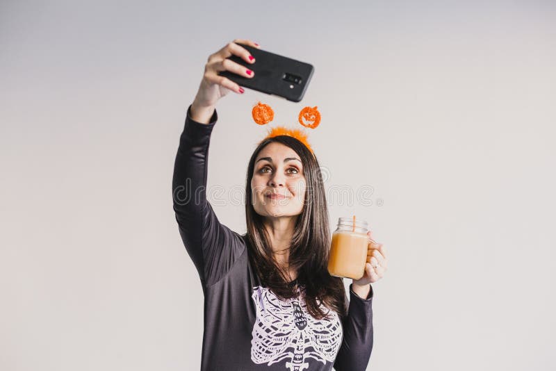 En ung vacker kvinna som dricker apelsinjuice och tar en selfie med mobiltelefon. Med ett svart och vitt skelett arkivfoton