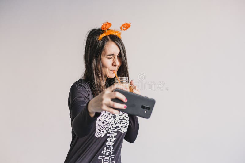 En ung vacker kvinna som dricker apelsinjuice och tar en selfie med mobiltelefon. Med ett svart och vitt skelett royaltyfri fotografi