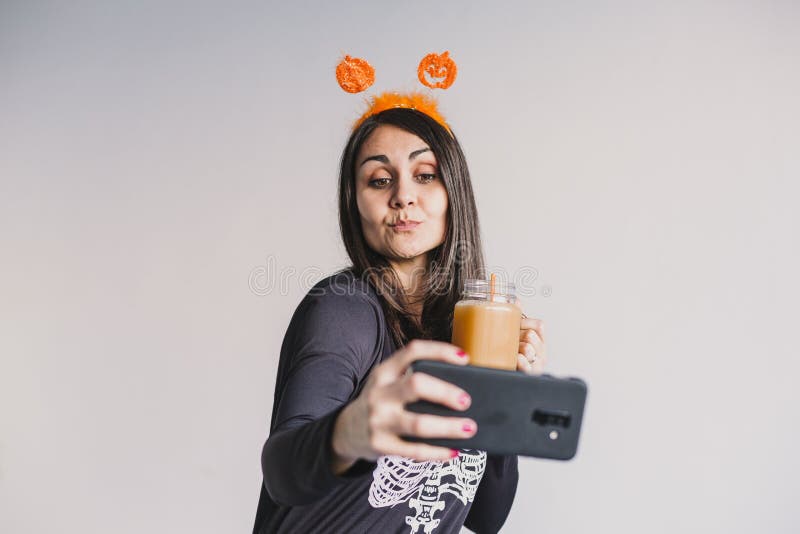 En ung vacker kvinna som dricker apelsinjuice och tar en selfie med mobiltelefon. Med ett svart och vitt skelett royaltyfri fotografi