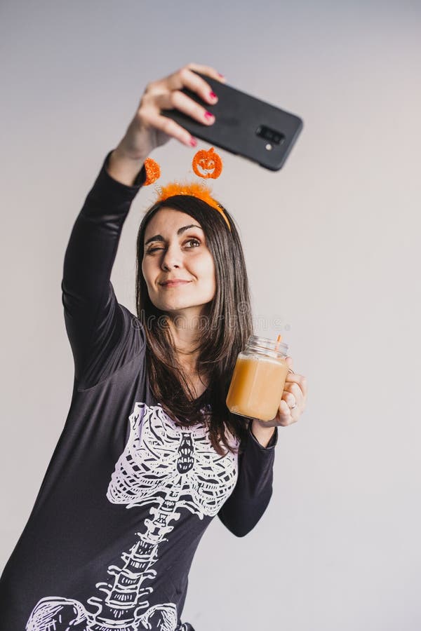 En ung vacker kvinna som dricker apelsinjuice och tar en selfie med mobiltelefon. Med ett svart och vitt skelett arkivbild