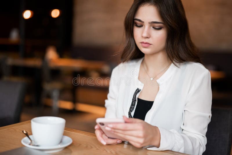 En ung vacker kvinna som kollar sin smartphone när hon dricker varmt kaffe i cafe-serien med multitasking och modern affärskvinna fotografering för bildbyråer En ung vacker kvinna som kollar sin smartphone när hon dricker varmt kaffe i cafe-serien med multitasking och modern affärskvinna fotografering för bildbyråer