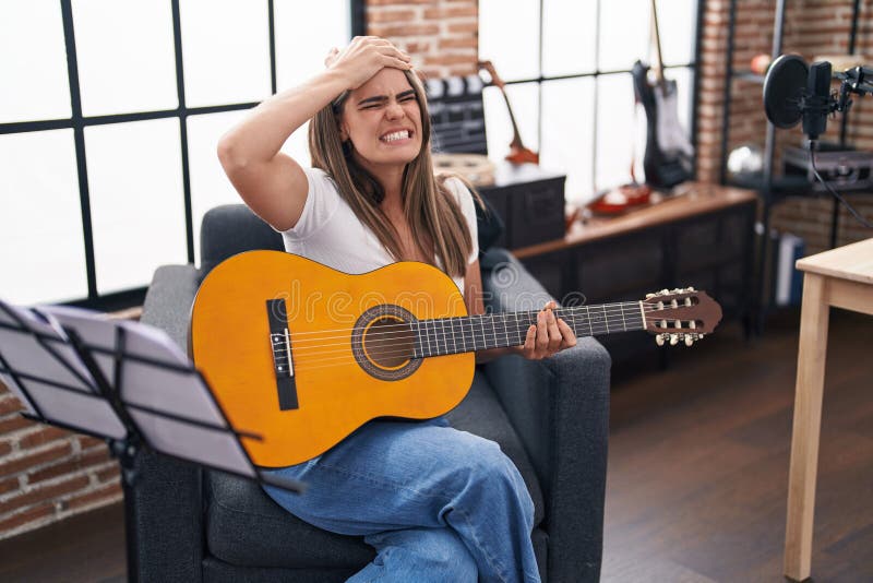 En ung vacker kvinna som spelar klassisk gitarr i musikstudion stressad och frustrerad med hand på huvudet överraskad och arg ansikte