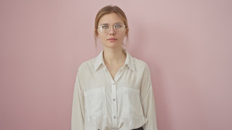 En ung vuxen kvinna med glasögon som bär en tillfällig skjorta står emot en rosa vägg som utesluter ett naturligt självsäkert utse royaltyfri foto