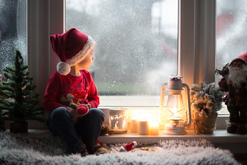 En vacker barnpojke som väntar på fönstret på julafton och letar efter julklaus royaltyfri fotografi
