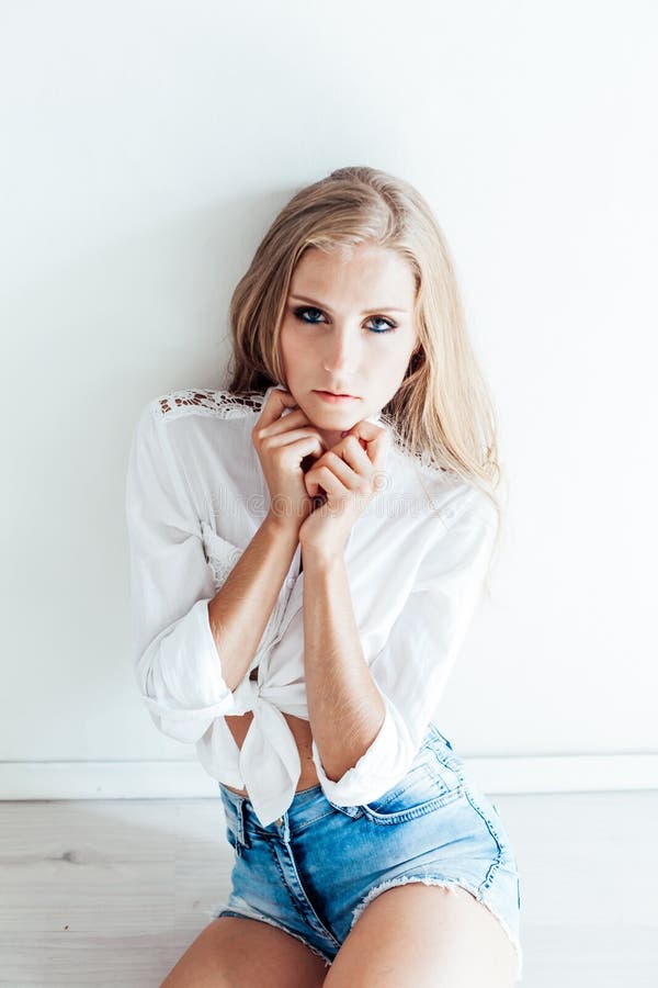 Beautiful blonde girl with blue eyes sitting on the floor in a white room. Beautiful blonde girl with blue eyes sitting on the floor in a white room