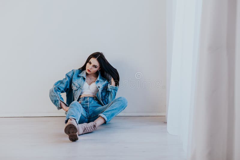 Beautiful girl in jeans clothes sitting on the floor in a white room 1. Beautiful girl in jeans clothes sitting on the floor in a white room 1
