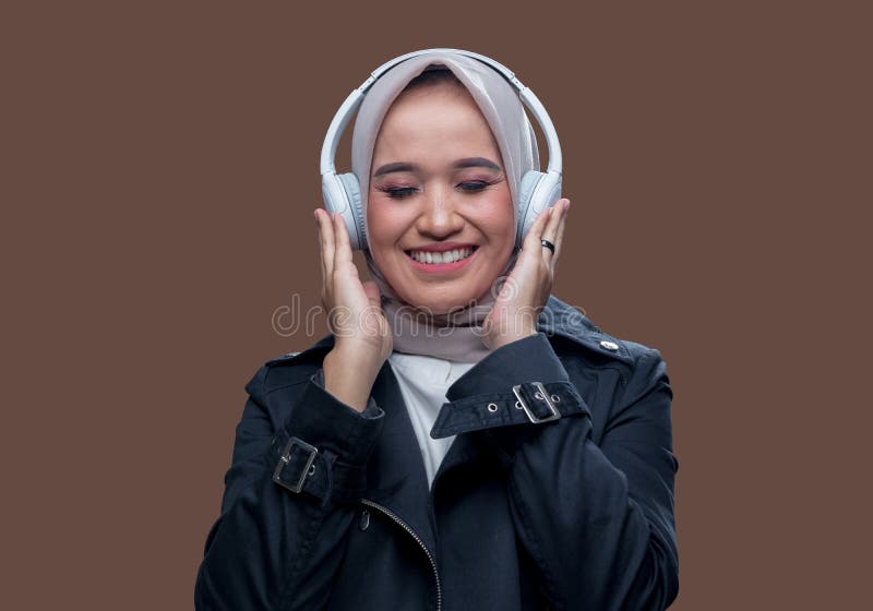 En vacker kvinna i hijab lyssnade på musik med hjälp av trådlösa hörlurar med ett leende uttryck medan hon blundade arkivbild
