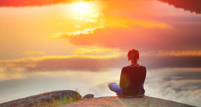 En vacker kvinna sitter i en lägenhet på en lotus på hög plats med en fantastisk syn på solnedgången i sjön yoga meditation kundal fotografering för bildbyråer