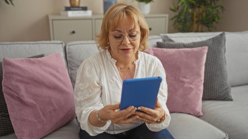 En vacker kvinna som använder en tablett i ett bekvämt vardagsrum hemma med moderna möbler och kuddar royaltyfria foton