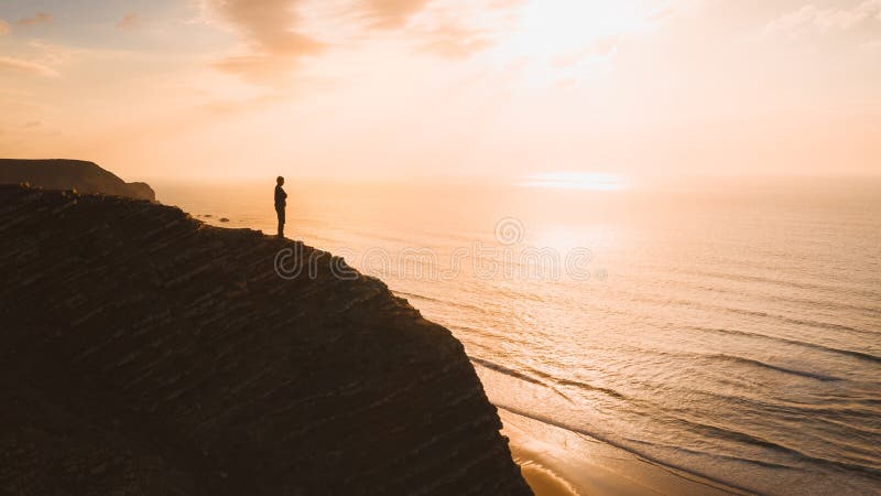 En vacker syn på en person som står på en klippa över havet vid solnedgången i Algarve, Portugal arkivfoto