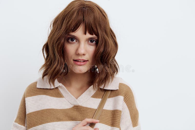 En vacker, trevlig kvinna i en stripe svettare tittar på kameran som står på vit bakgrund royaltyfri bild