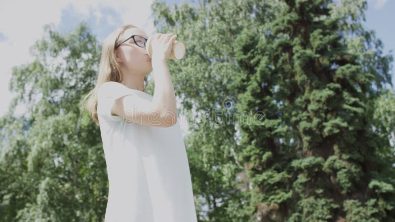 En vacker ung blondinsk kvinna dricker kaffe för att gå från en papp i papp på varm sommardag och drömt om att titta bort från kam