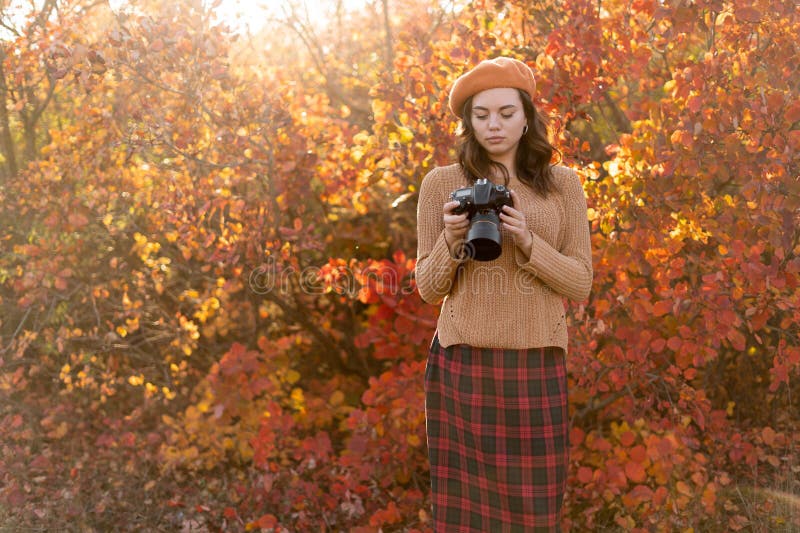 En vacker ung fotograf tar bilder med en dslr-kamera i höstskogen. ler flicka som njuter av höstväder arkivfoto