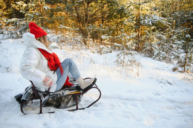 En vacker ung kvinna som bär varma vinterkläder som sitter på ett kölvatten och glider ner i kullen och roar sig på en snövinter arkivbild