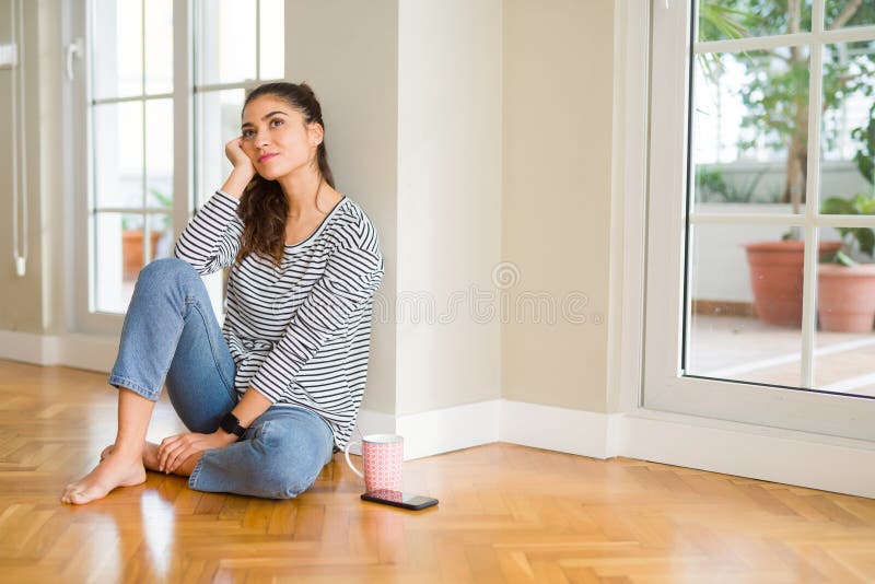 En vacker ung kvinna som ler trygg och tänker positivt på att sitta hemma på golvet på morgonen arkivbild