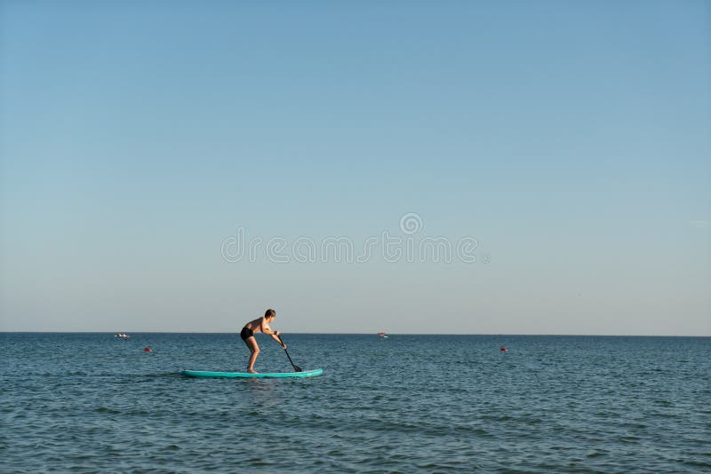 En 12-årig pojke lär sig att stå på ett avstigningsbord i havet nära kusten. royaltyfria bilder