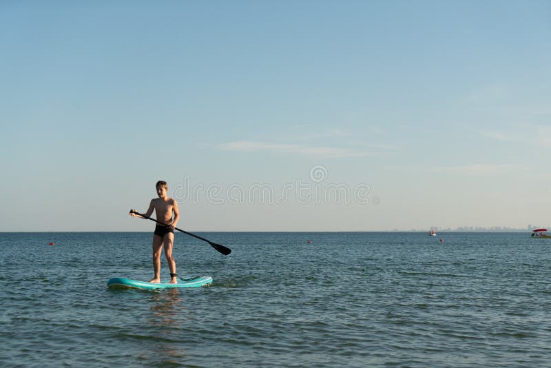 En 12-årig pojke lär sig att stå på ett avstigningsbord i havet nära kusten. arkivfoton