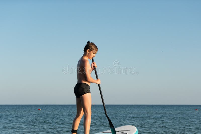 En 12-årig pojke lär sig att stå på ett avstigningsbord i havet nära kusten. royaltyfri fotografi