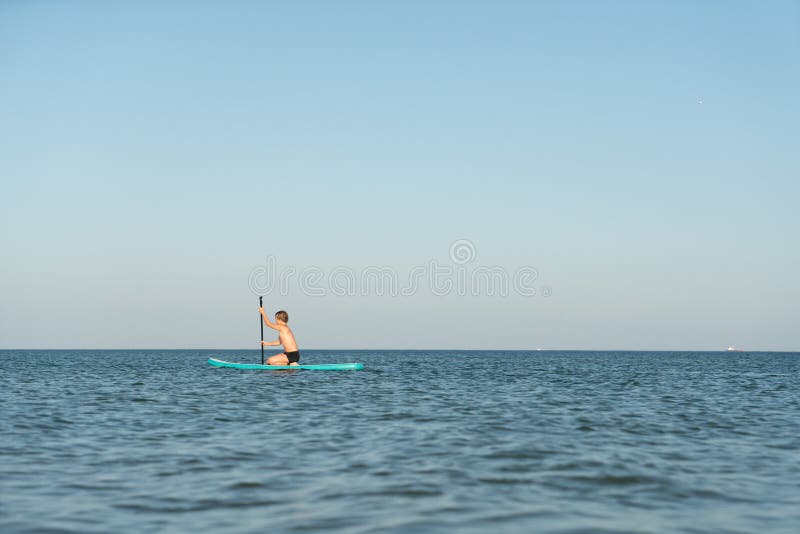 En 12-årig pojke lär sig att stå på ett avstigningsbord i havet nära kusten. arkivfoto