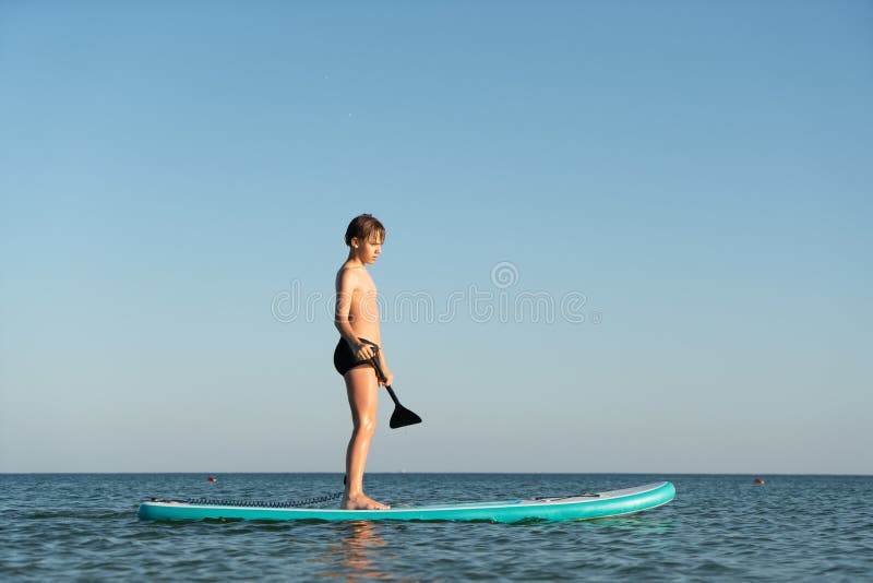 En 12-årig pojke lär sig att stå på ett avstigningsbord i havet nära kusten. arkivfoto