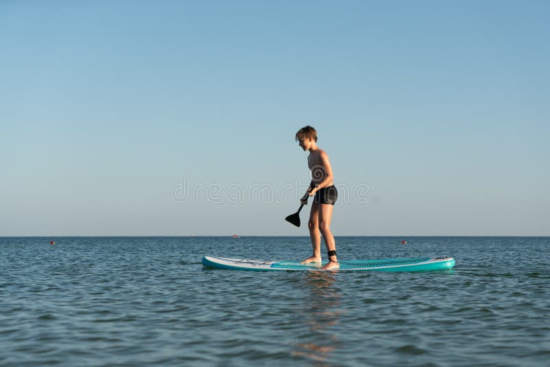 En 12-årig pojke lär sig att stå på ett avstigningsbord i havet nära kusten. royaltyfri fotografi