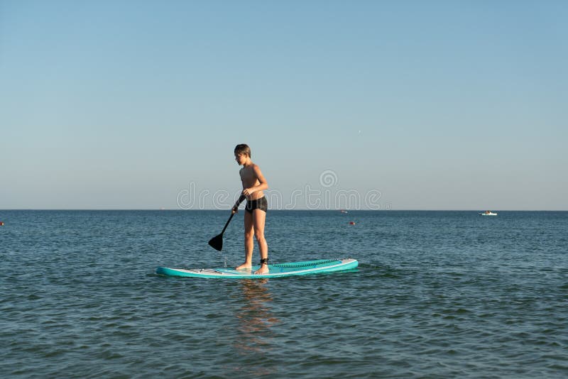 En 12-årig pojke lär sig att stå på ett avstigningsbord i havet nära kusten. royaltyfri bild