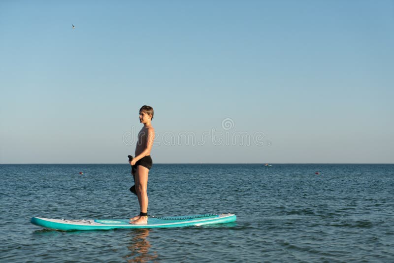 En 12-årig pojke lär sig att stå på ett avstigningsbord i havet nära kusten. arkivfoto