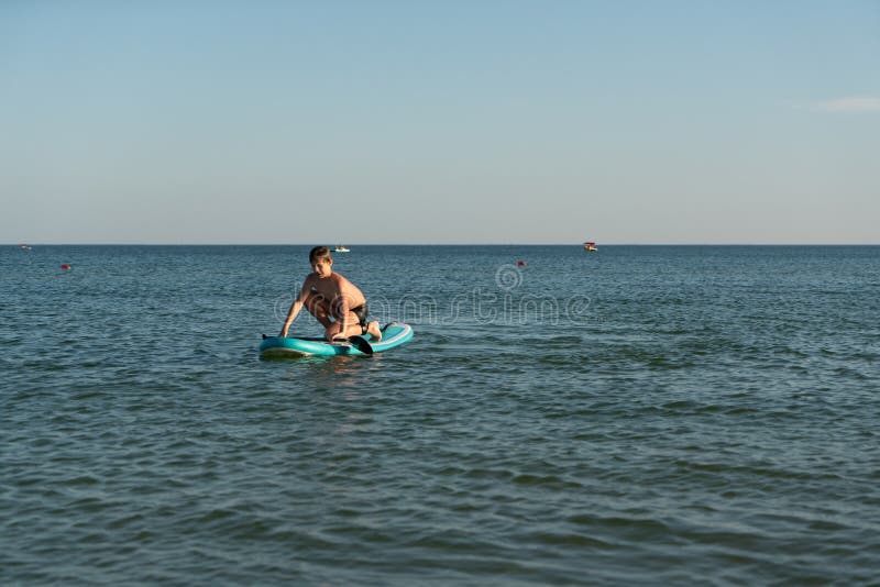 En 12-årig pojke lär sig att stå på ett avstigningsbord i havet nära kusten. royaltyfri fotografi