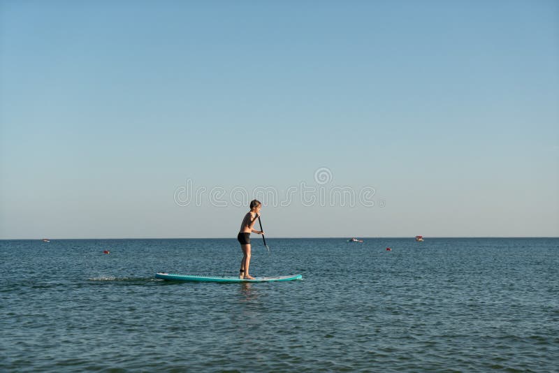 En 12-årig pojke lär sig att stå på ett avstigningsbord i havet nära kusten. arkivbild