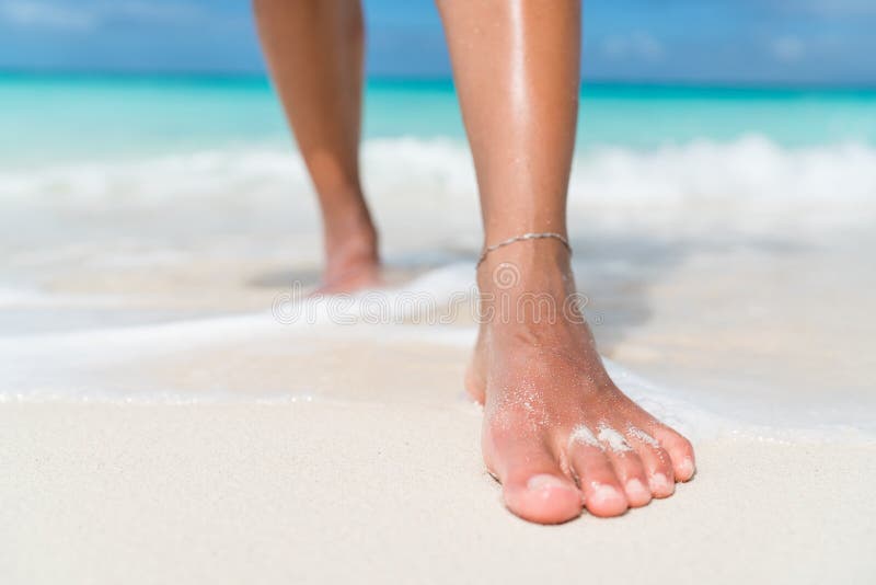 Encalhe o close up dos pés - mulher que anda em ondas de água