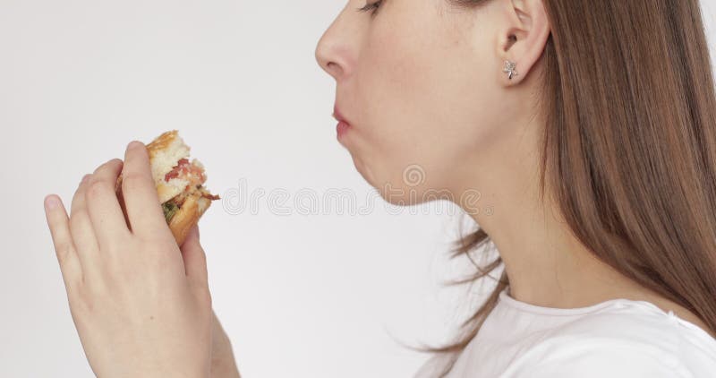 Encantadora mujer hambrienta come una gran hamburguesa y sonríe aislada en un fondo blanco