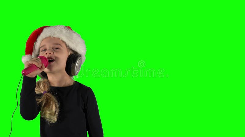 Encantadora niñita con micrófono cantando la canción de navidad. pantalla verde