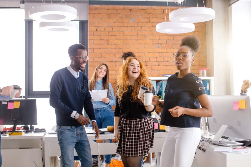 Encargados jovenes sonrientes que beben té en tiempo de la rotura en el lugar de trabajo imágenes de archivo libres de regalías Encargados jovenes sonrientes que beben té en tiempo de la rotura en el lugar de trabajo imágenes de archivo libres de regalías