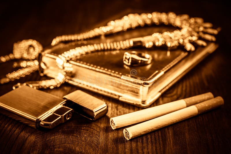 Golden lighter with a leather diary and cigarettes with jewellery on a mahogany table. Focus on the cigarettes. Golden lighter with a leather diary and cigarettes with jewellery on a mahogany table. Focus on the cigarettes