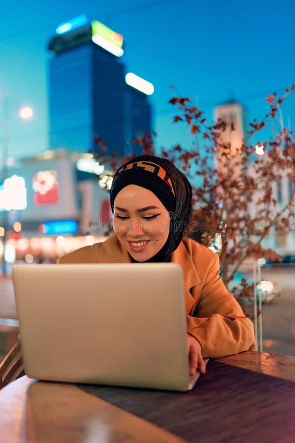 în atmosfera încântătoare a unui peisaj nocturn al orașului, o hijabclad-girl îngropată în laptop-ul ei crează o fascinantă royalty free stock image