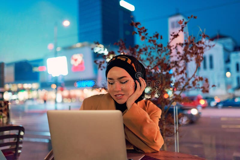 în atmosfera încântătoare a unui peisaj nocturn al orașului, o hijabclad-girl îngropată în laptop-ul ei crează o fascinantă stock images
