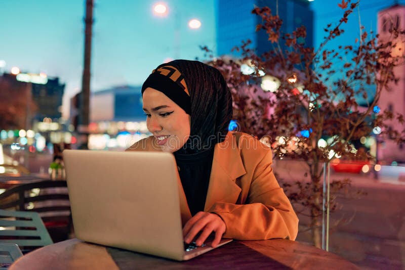 în atmosfera încântătoare a unui peisaj nocturn al orașului, o hijabclad-girl îngropată în laptop-ul ei crează o fascinantă royalty free stock photos