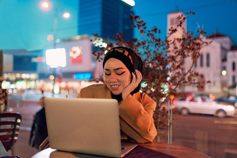 în atmosfera încântătoare a unui peisaj nocturn al orașului, o hijabclad-girl îngropată în laptop-ul ei crează o fascinantă royalty free stock photo
