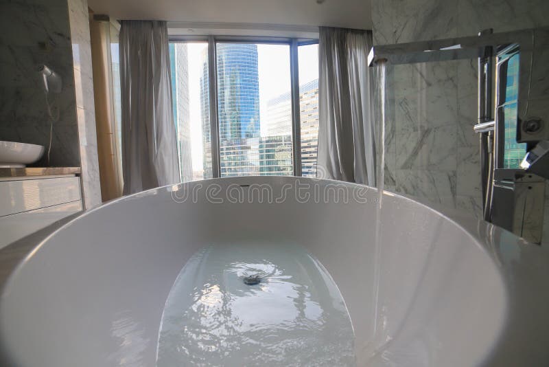 Enchimento da água na banheira moderna no interior do banheiro - construções de vidro modernas em um fundo imagens de stock Enchimento da água na banheira moderna no interior do banheiro - construções de vidro modernas em um fundo imagens de stock
