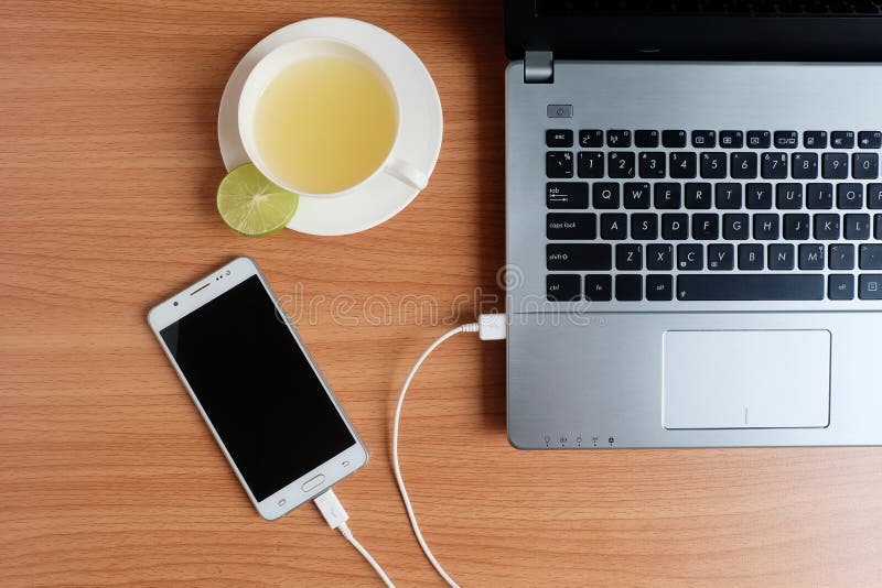 Enchufe el cargador del cable USB del teléfono móvil con un ordenador portátil y recientemente un zumo de lima en una taza blanca fotografía de archivo libre de regalías