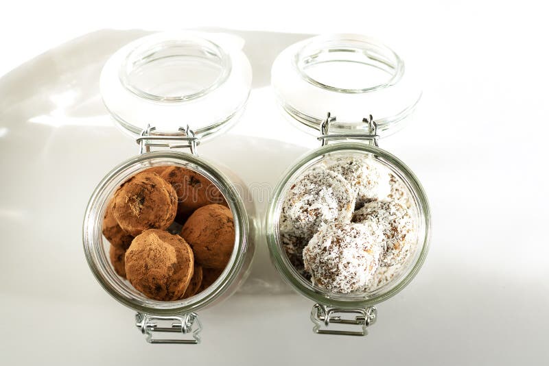 Energiebälle in einem Glas mit Joch Zwei Container mit unterschiedlichen Gerichten Schatten im Tageslicht Oberansicht. Gesunde Snacks, gesunde Lebensmittel Nahrungsergänzung Leerstelle kopieren, weißer Background, vertikale Ausrichtung Energiebälle in Kokos- und Kakaopulver